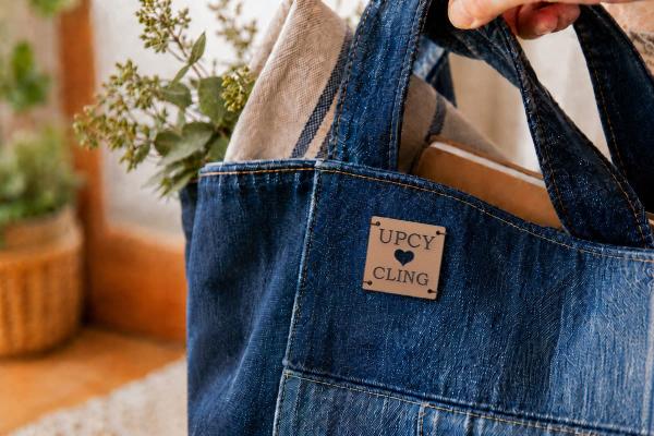Square, light brown cactus leather label with the inscription "UPCYCLING" and a die-cut heart on a denim tote bag.