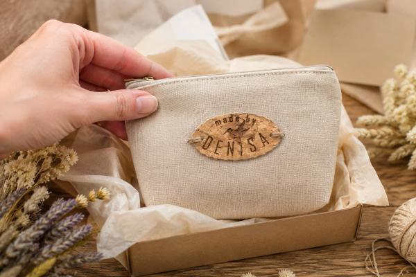 Oval cork label reading "made by Denisa" stitched to a beige fabric pouch.