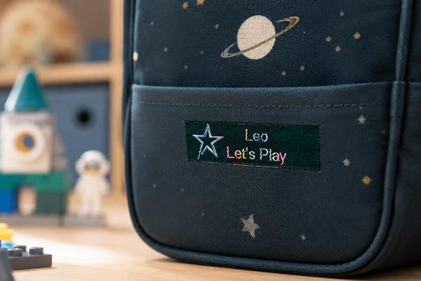 Moss green cotton label with rainbow lettering on kids backpack